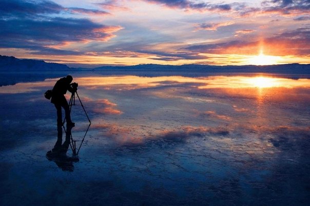 Man taking picture of a sunset over water
