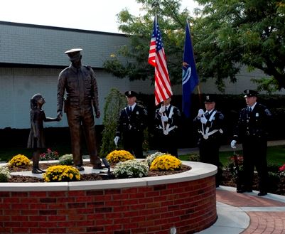 Police officers viewing a statue of a young girl holing an officer's hand. 
