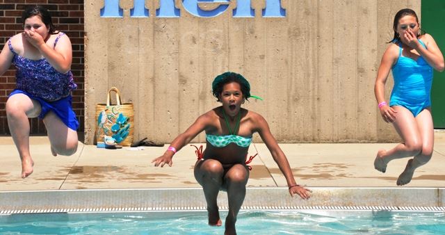 Three girls jumping into a swimming pool.